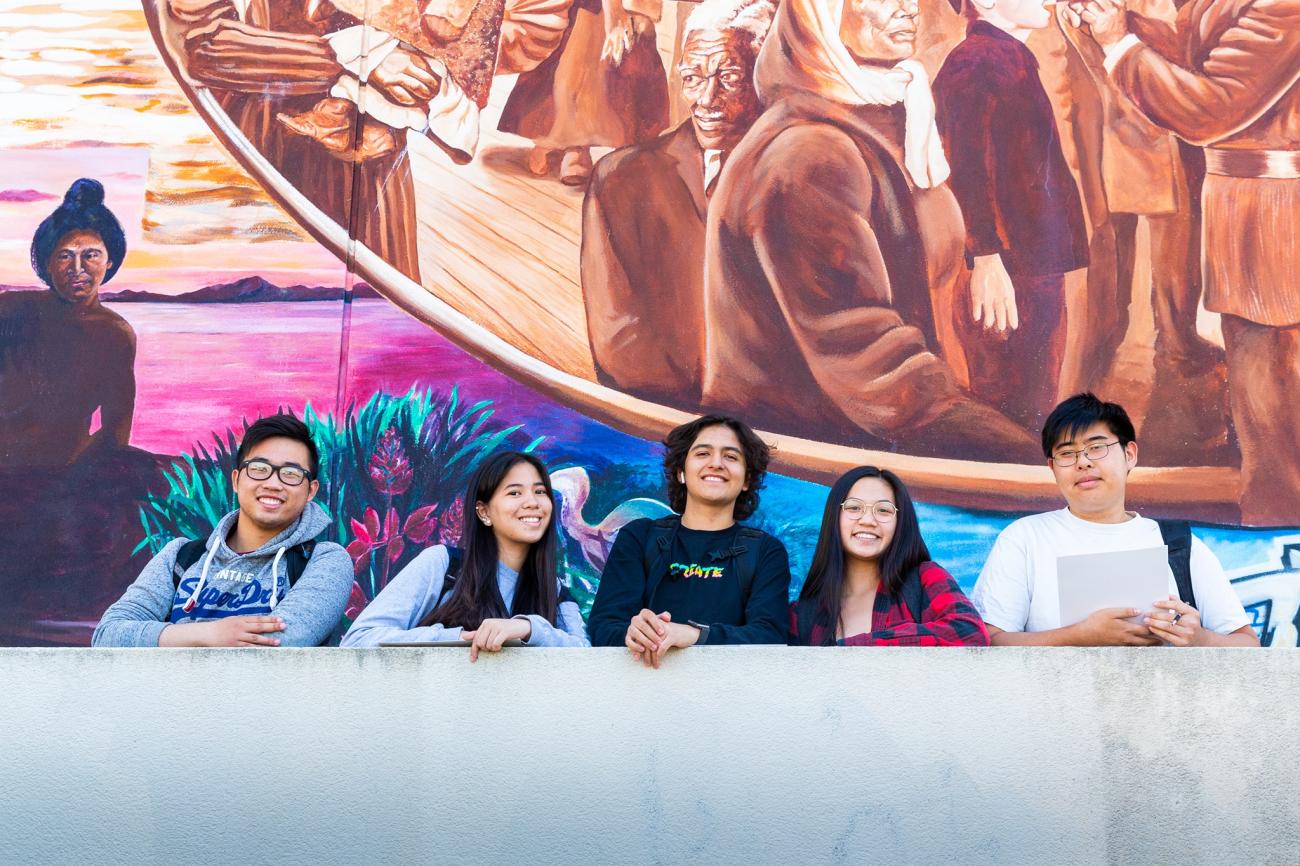 Diverse group of teens smile in front of mural