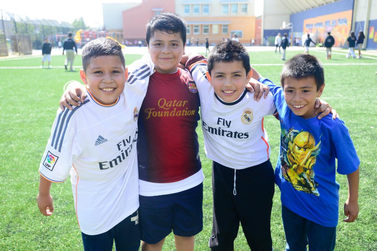 Four boys with their arms around each other on soccer field